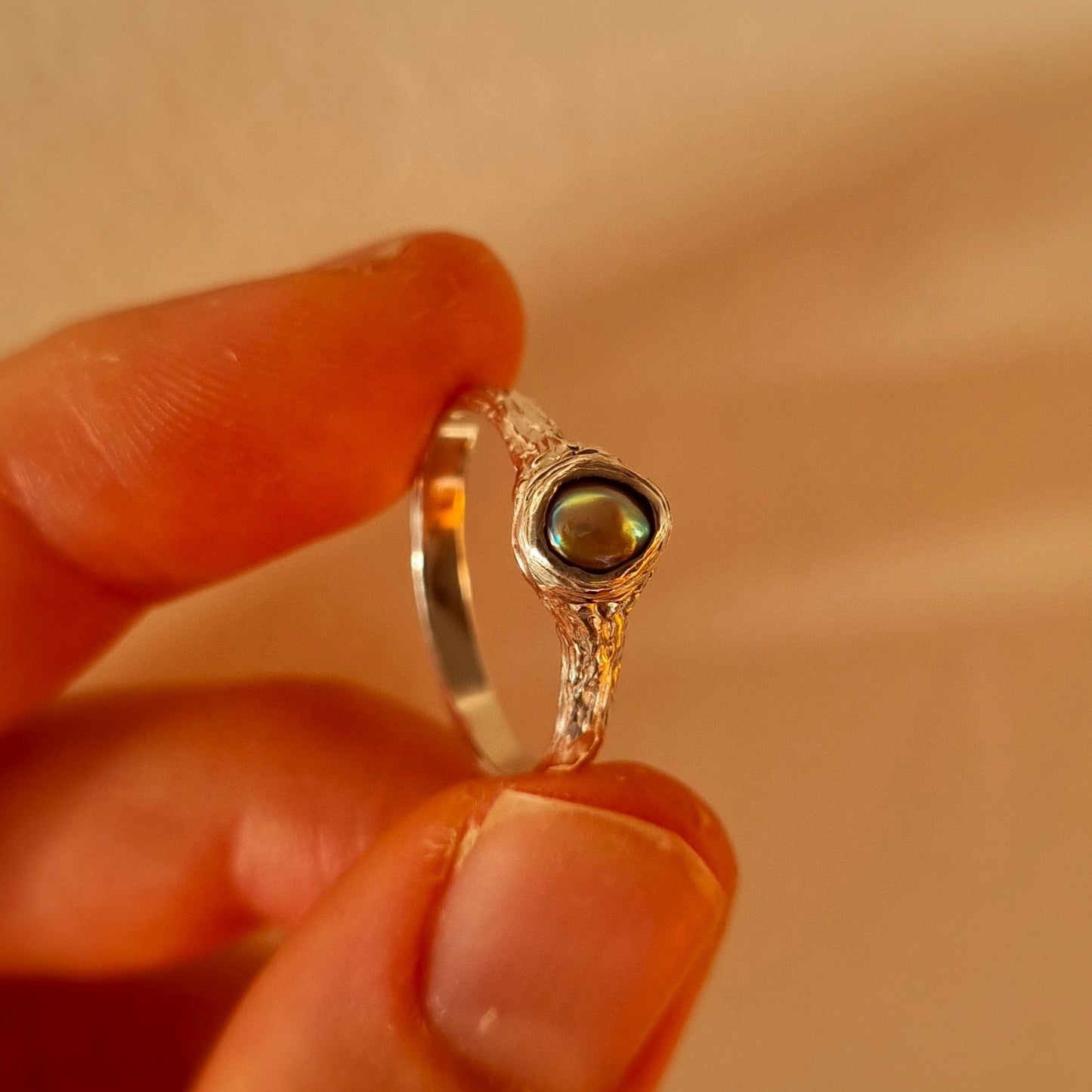 Silver ring with paua pearl held between fingers. Elizabeth French Jewellery
