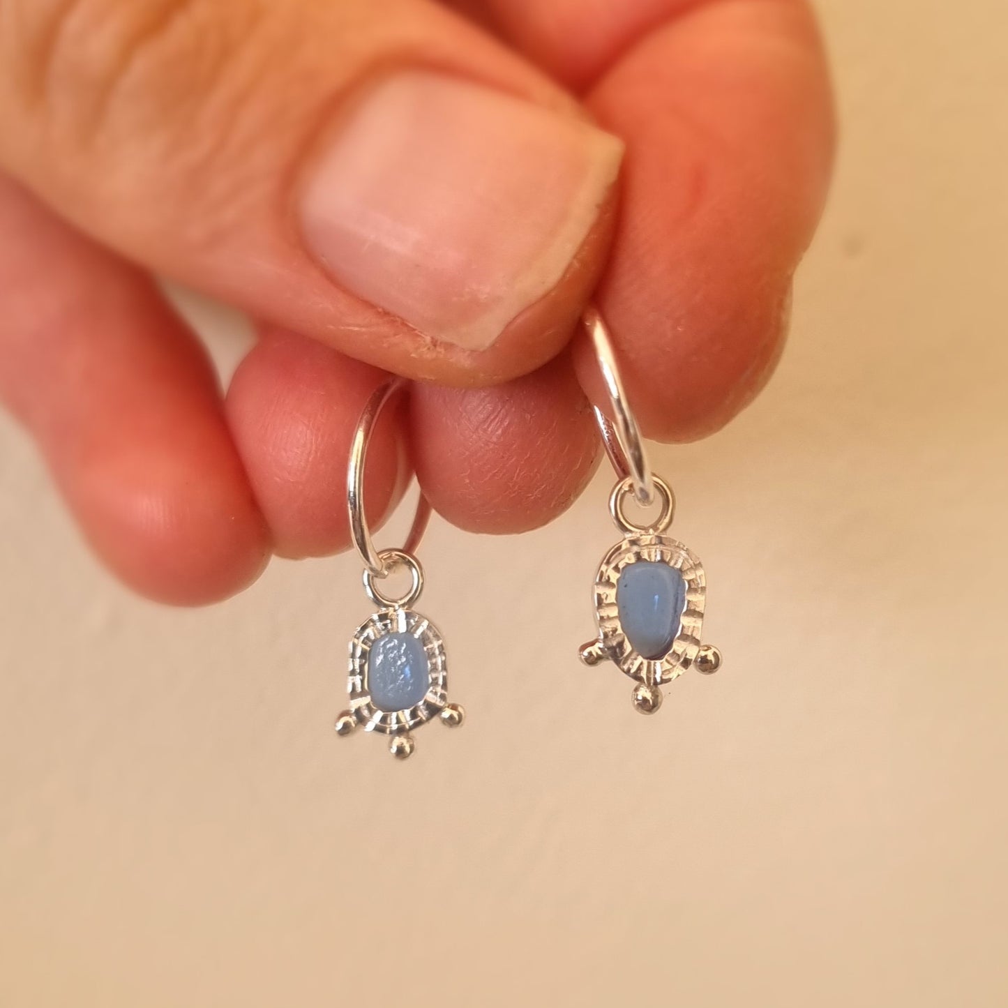 Silver earrings with blue stones held between fingers on a beige background