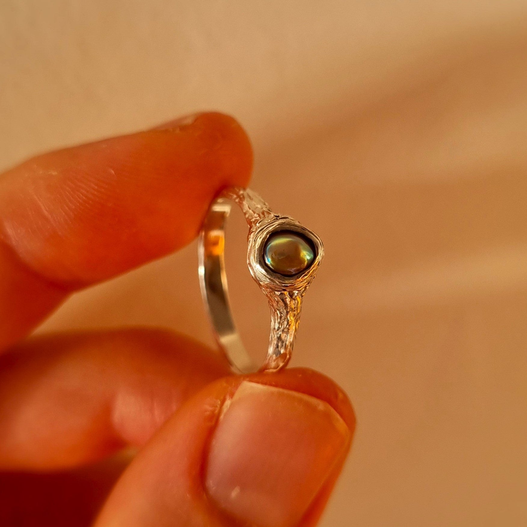 Silver ring with paua pearl held between fingers. Elizabeth French Jewellery