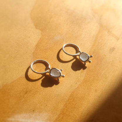 Pair of silver hoop earrings with teardrop-shaped stones on a wooden surface